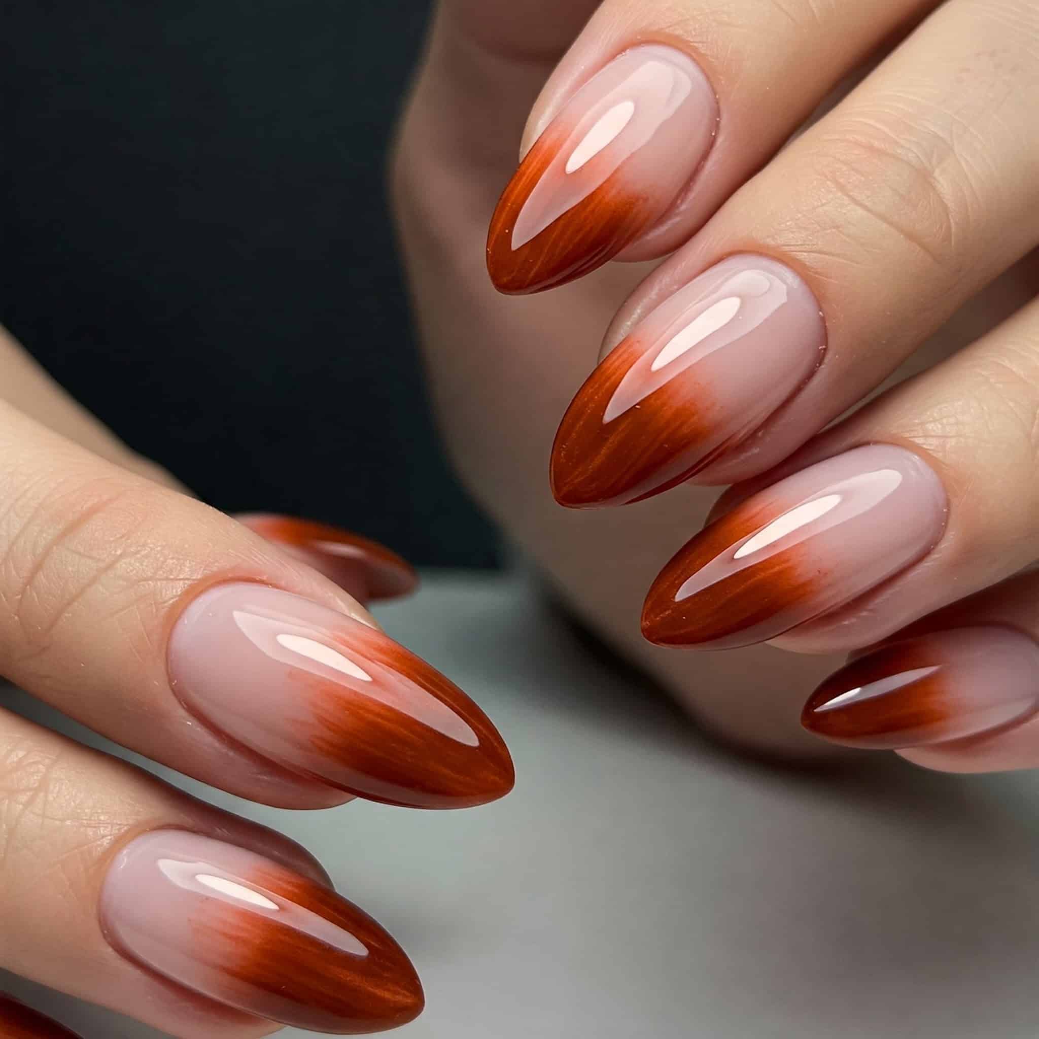 Close-up of hands with glossy almond-shaped nails featuring a gradient from nude to vibrant red.