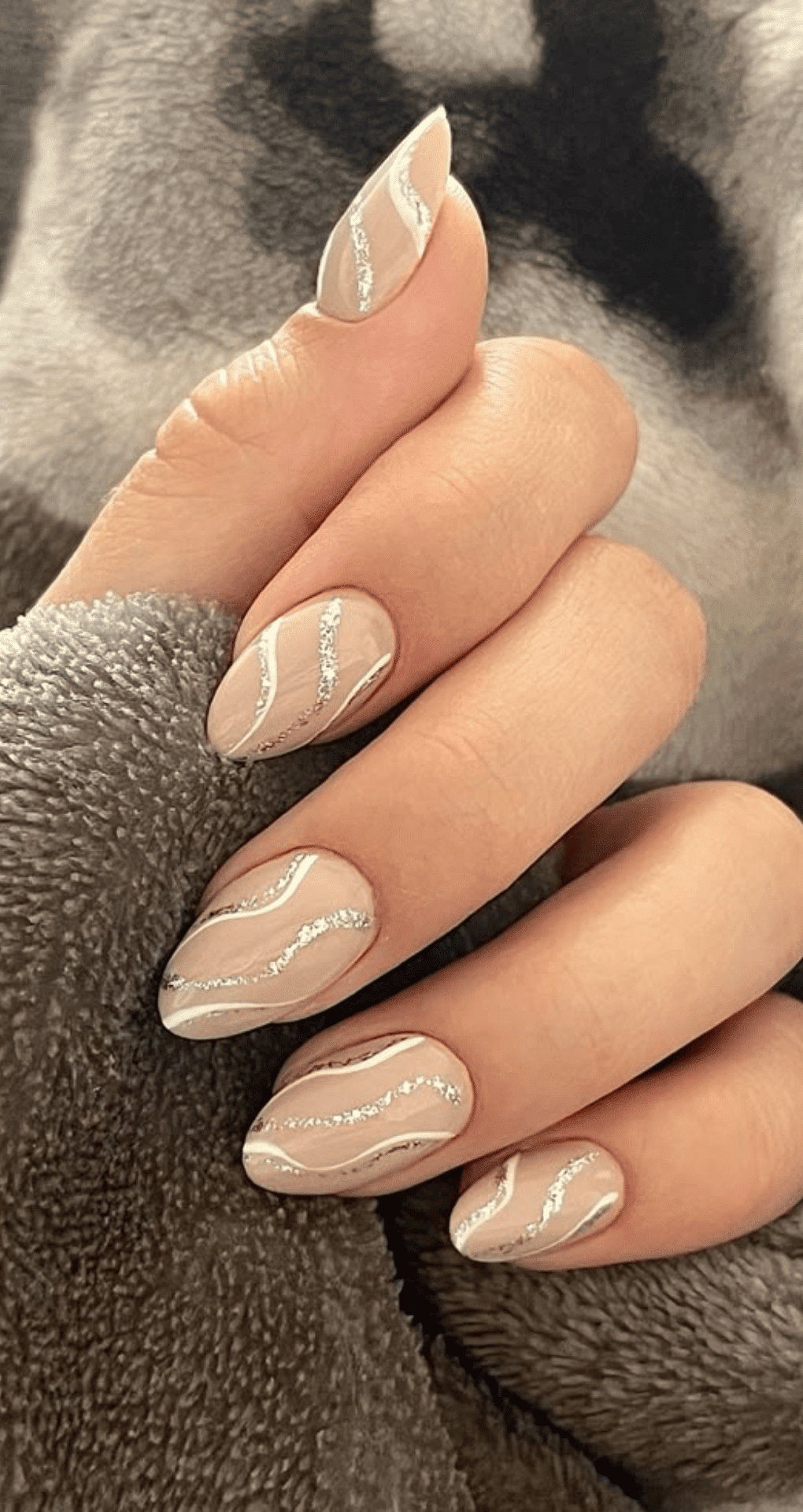 Almond nails with nude base decorated with silver wavy lines across each nail creating flowing effect