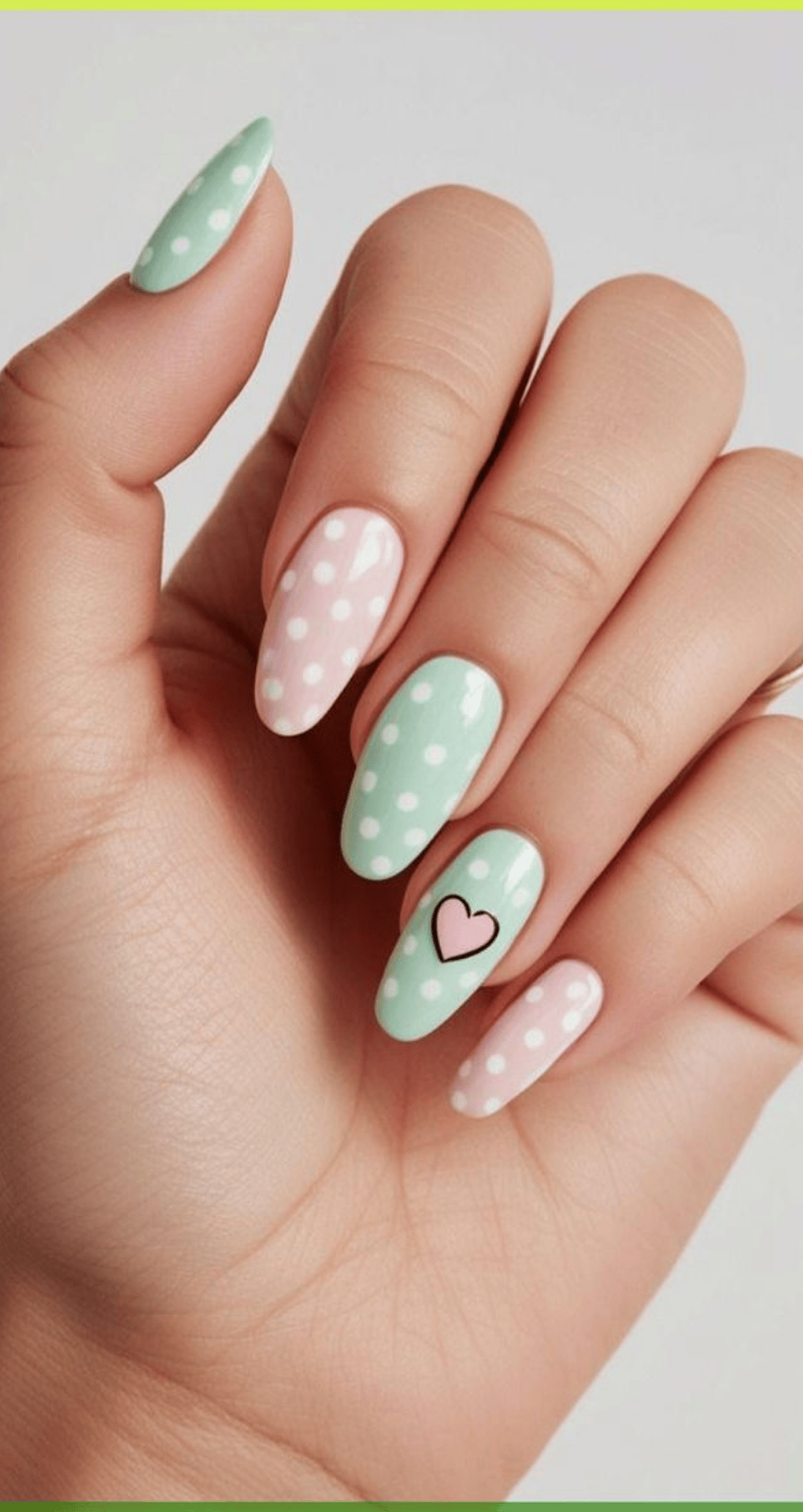 Almond nails painted pastel green and pink with white polka dots and black heart accent on middle nail