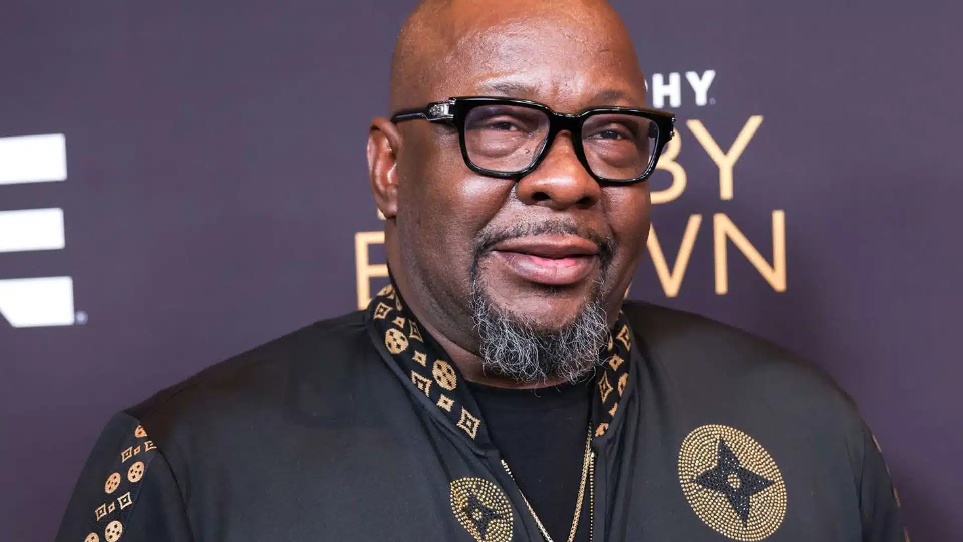 Bobby Brown poses for a photo in a black jacket with gold accents
