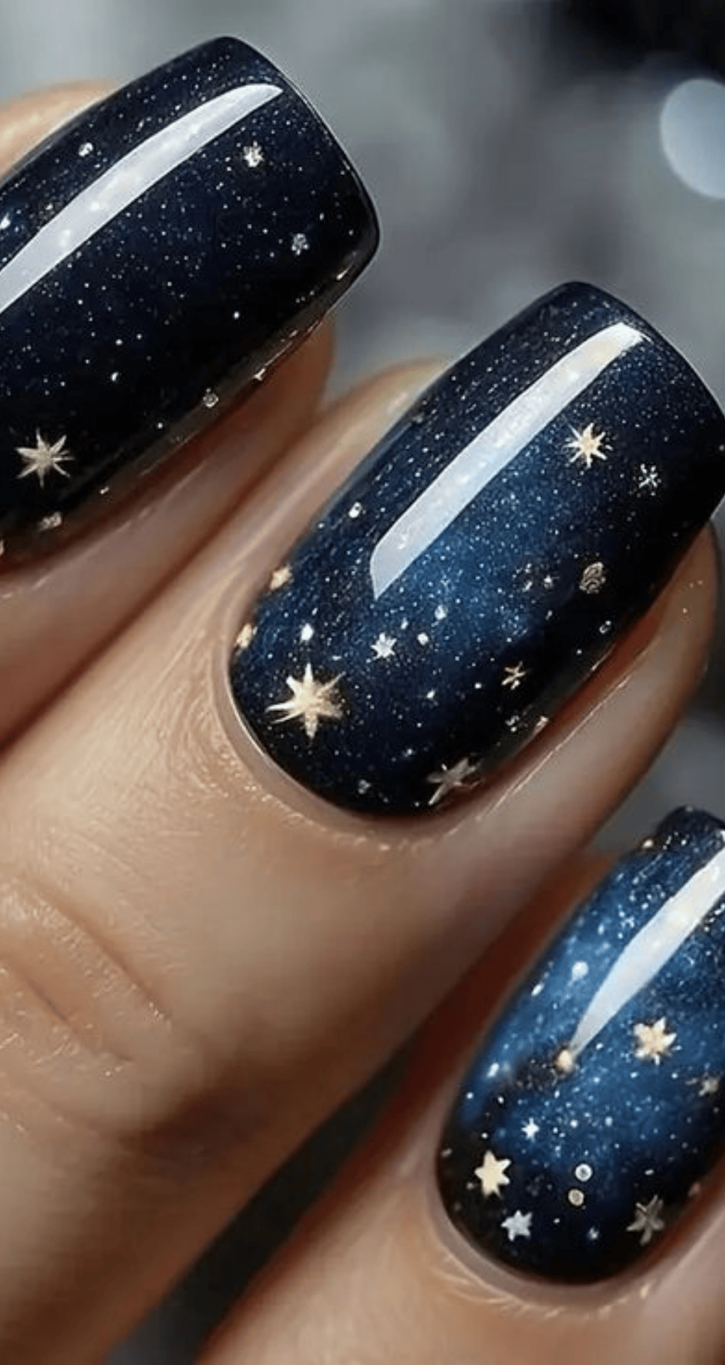 Almond nails painted dark navy with tiny white specks and gold star accents resembling a night sky