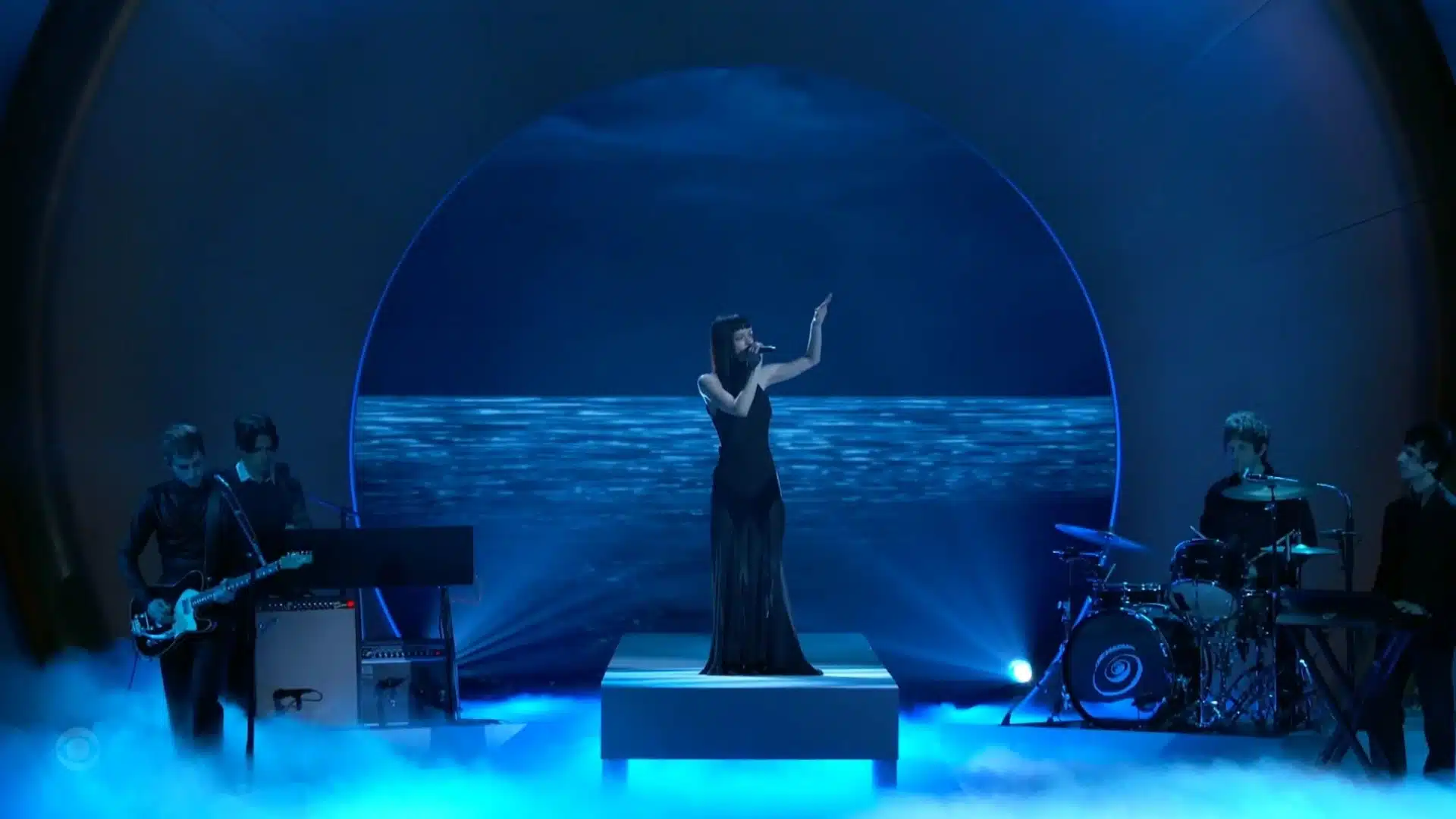 The Marias at the Grammys performs on stage with a backdrop of water and a blue, circular light