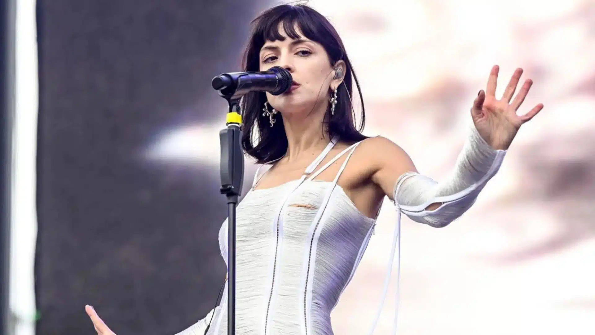 Artist María Zardoya performs on stage wearing a white dress and arm cast