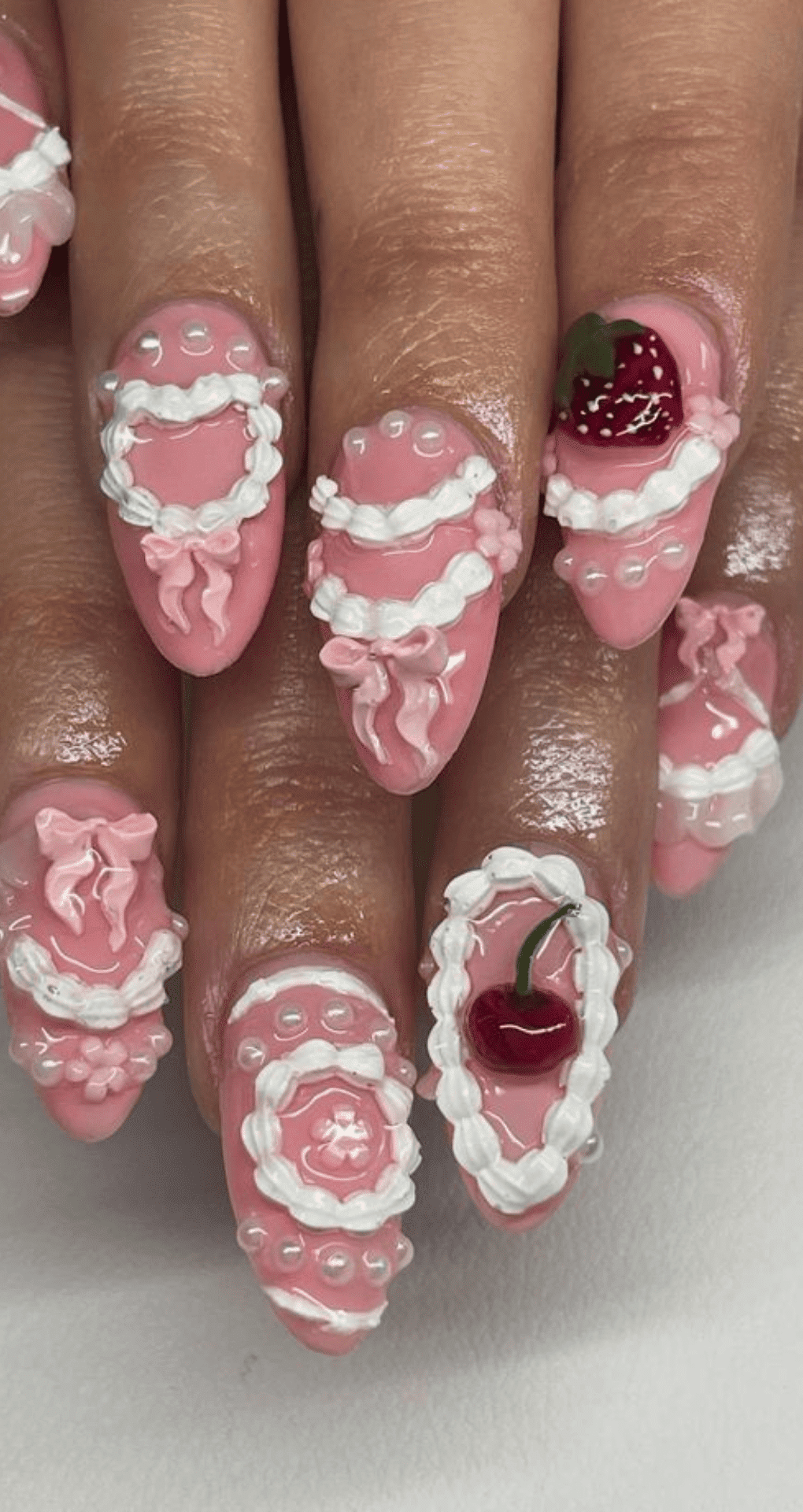 Almond shaped nails with bright pink base and 3d designs including bows roses pearls and fruit