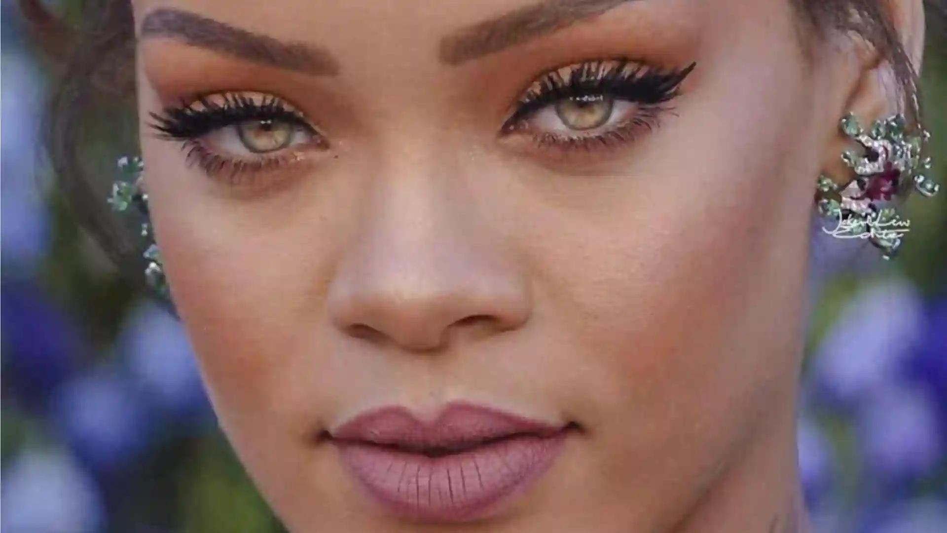 Close-up of a Rihanna's face with green eyes, dramatic makeup, and an ornate earring.