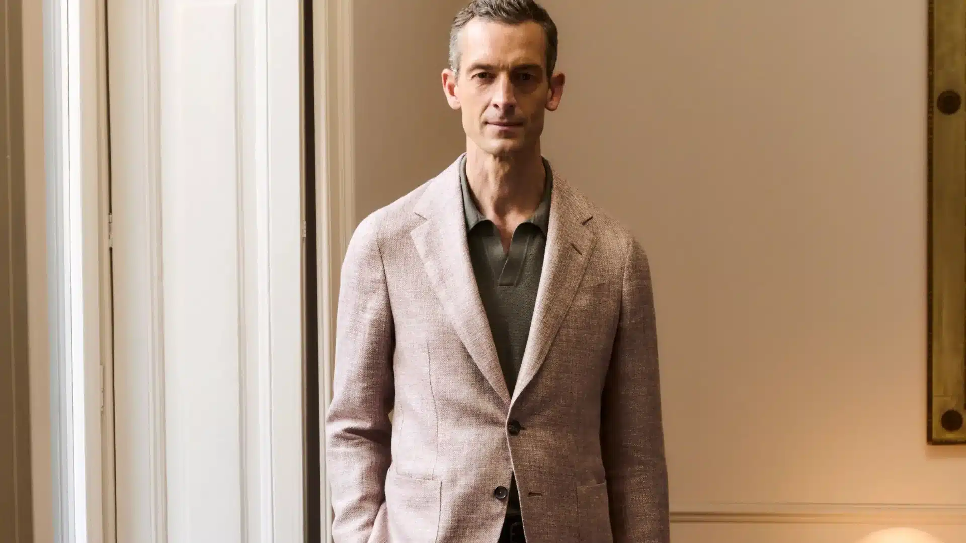Man wearing a light pink Zegna's linen blazer over a grey polo shirt stands