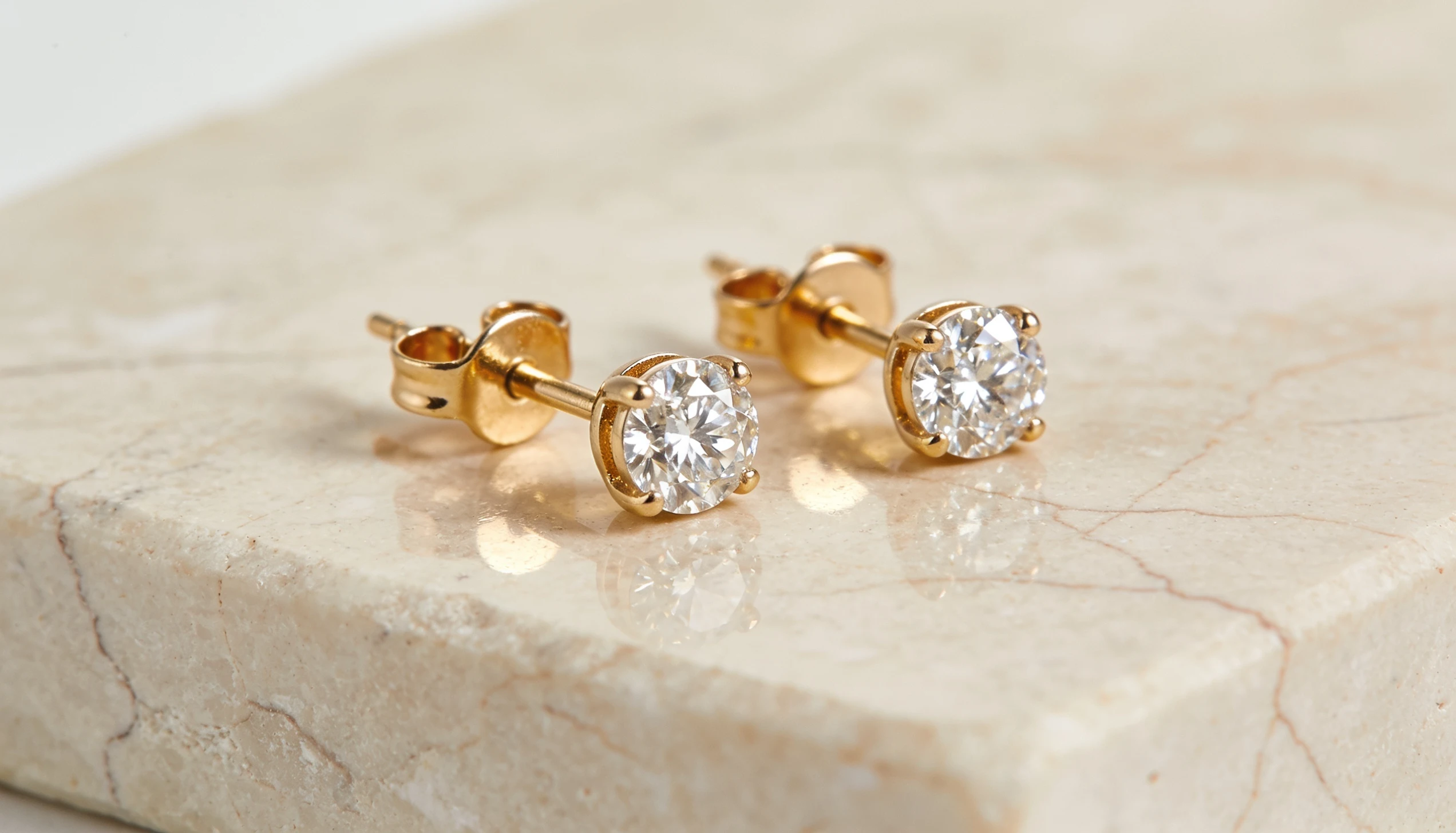 Gold stud earrings with round clear gemstones on a polished marble surface showcasing classic minimalist jewelry design and sparkle