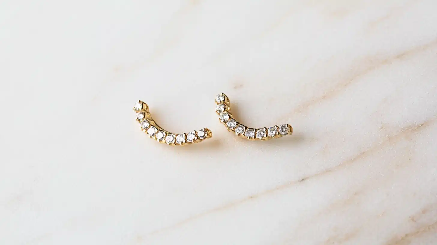 Gold climber earrings with sparkling crystal accents arranged in a curved design displayed on a marble surface featuring modern minimalist jewelry style