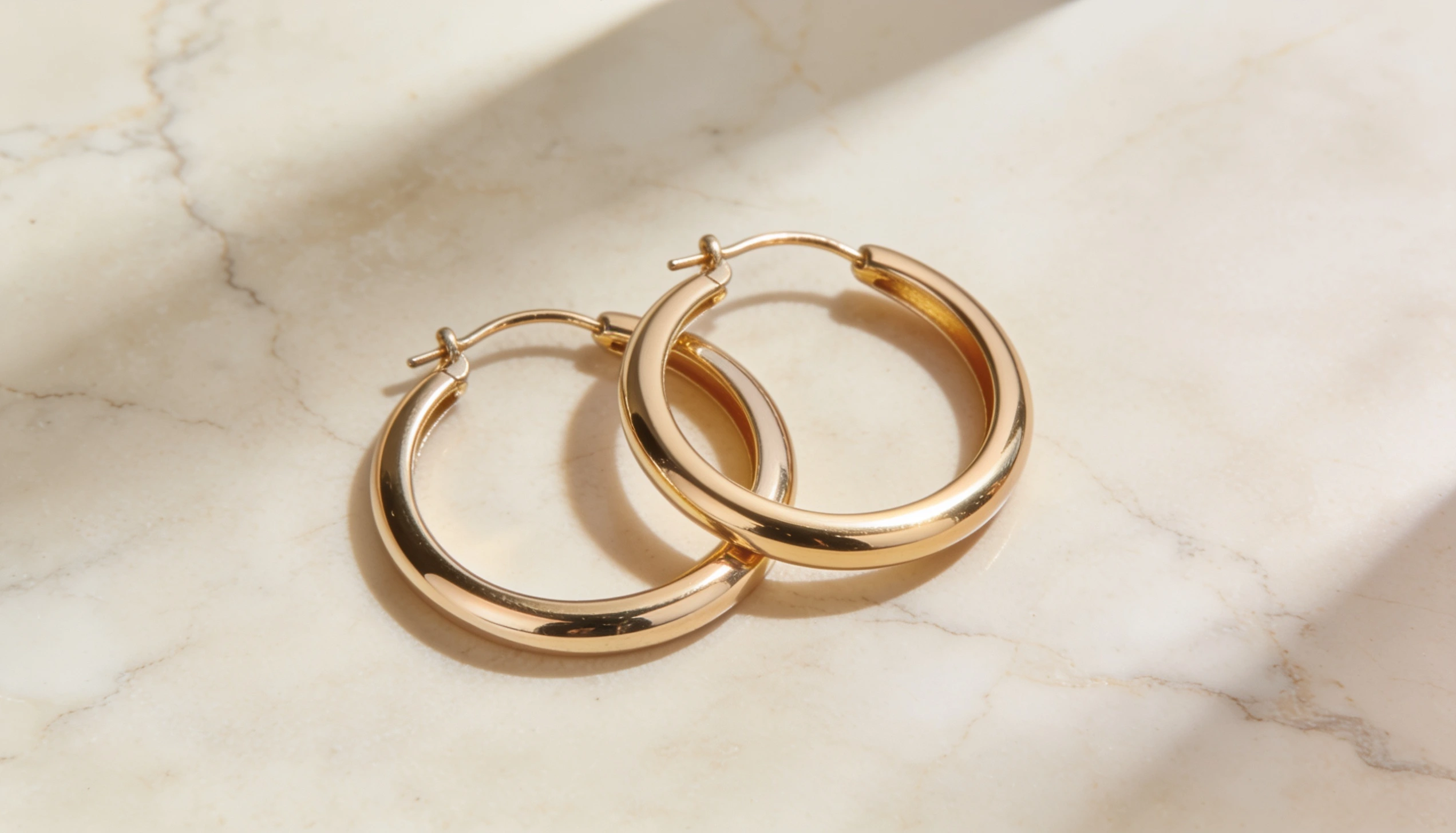 Classic gold hoop earrings with a polished finish resting on a marble surface highlighting timeless everyday jewelry style and elegance