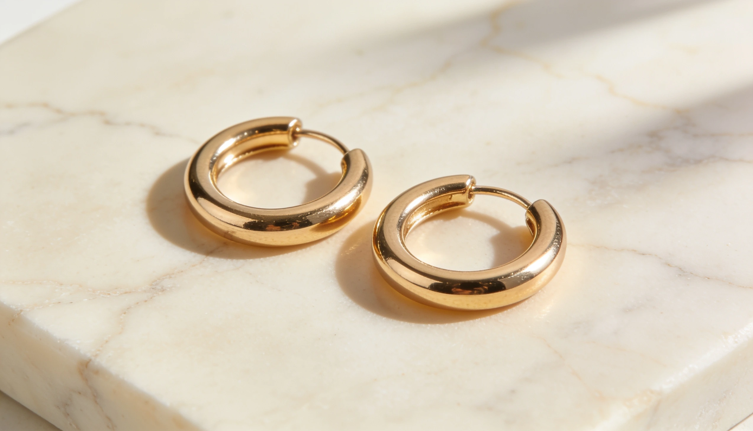 Gold huggie earrings with a smooth polished finish displayed on a marble surface featuring a modern everyday jewelry style and shine