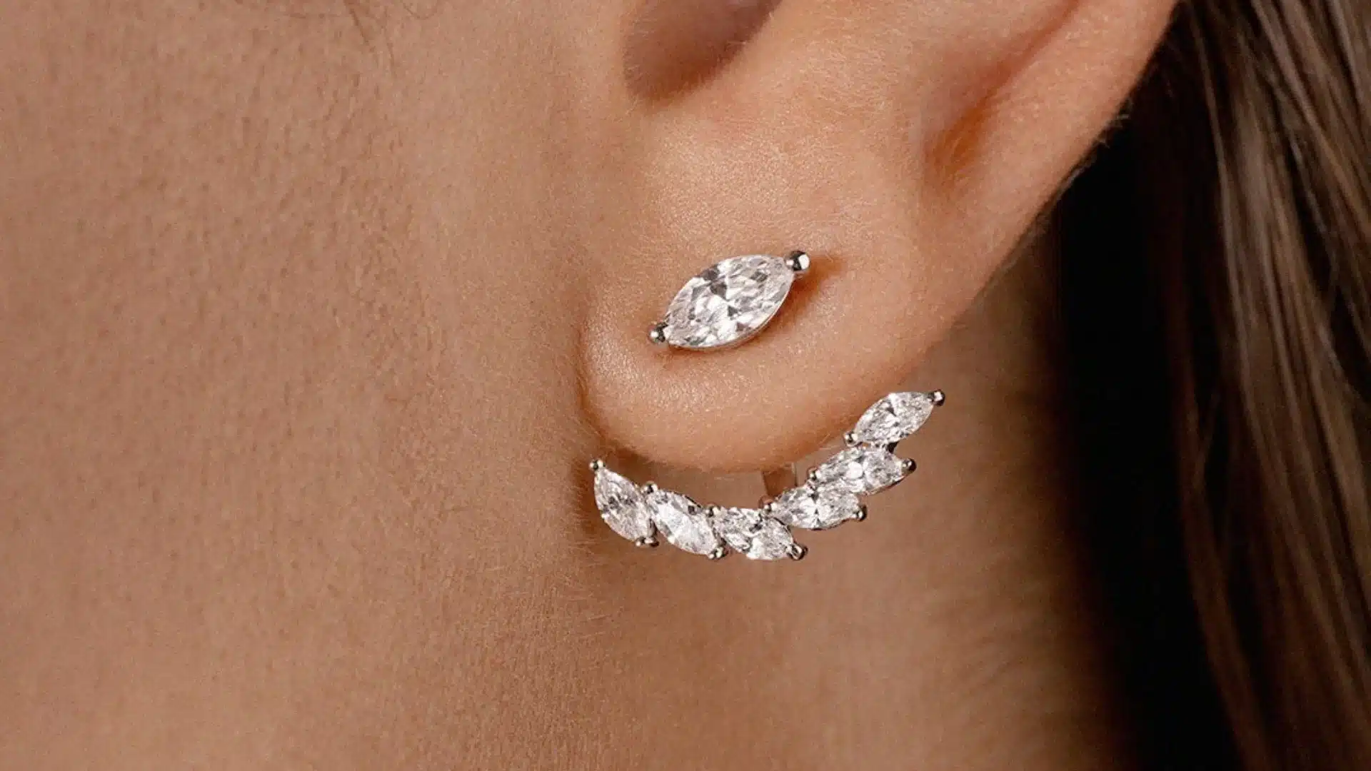 Close view of an ear wearing silver jacket earrings with sparkling marquise cut stones creating a curved layered design beneath the earlobe