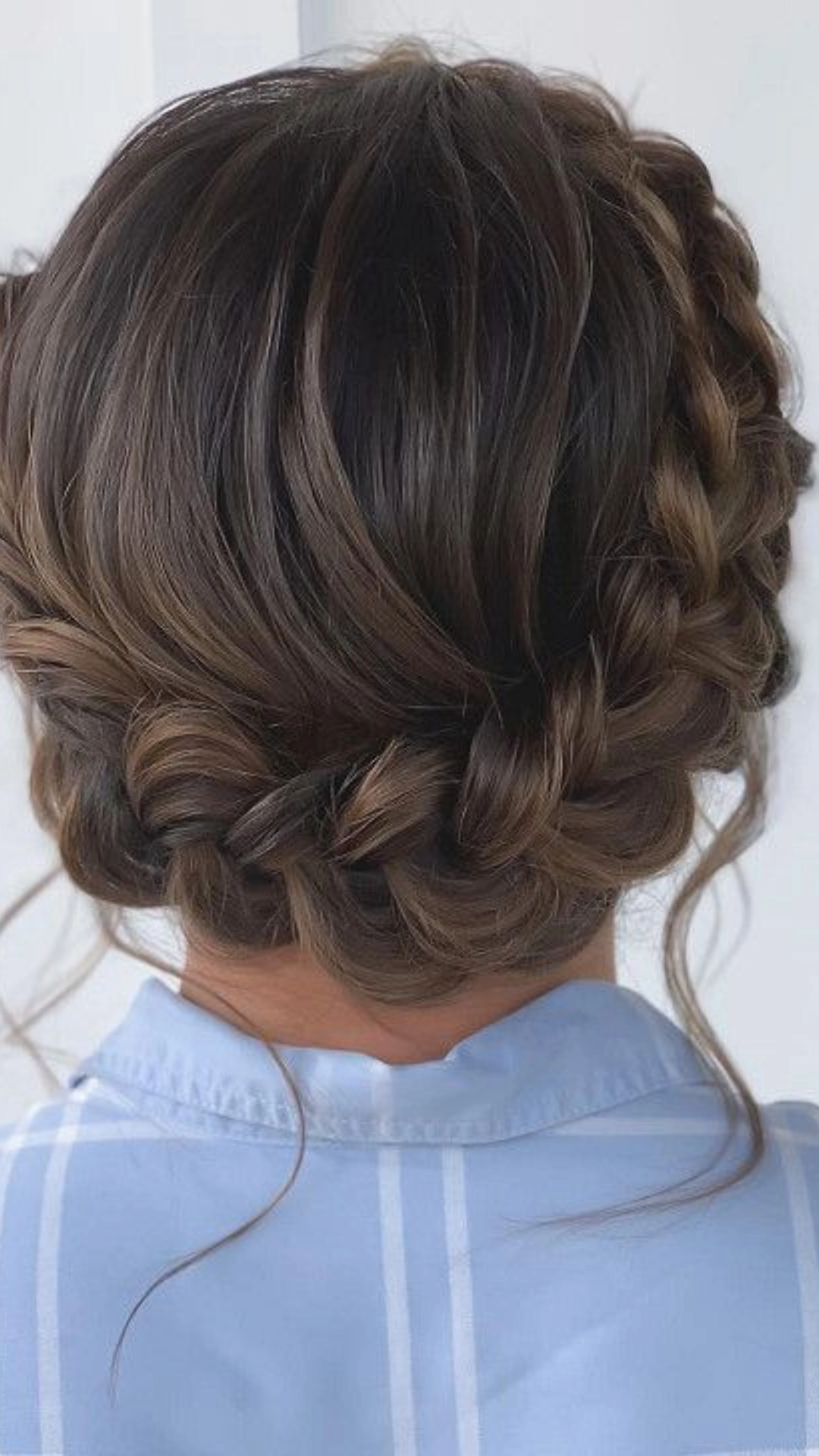 Braided updo with loose curled strands framing the neck