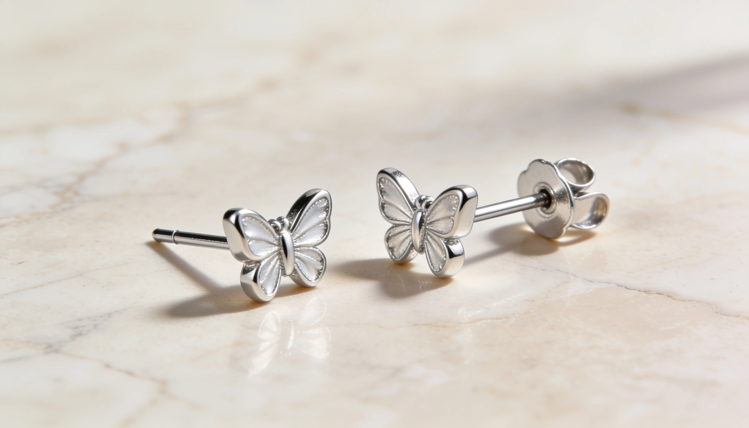 Silver butterfly stud earrings with butterfly push backs displayed on a marble surface showcasing secure classic earring backing for everyday wear