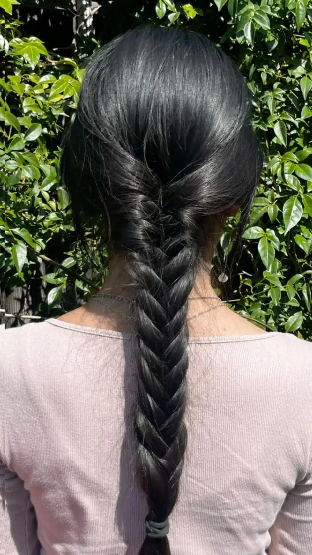 Fishtail braid styled into a low ponytail against a green backdrop