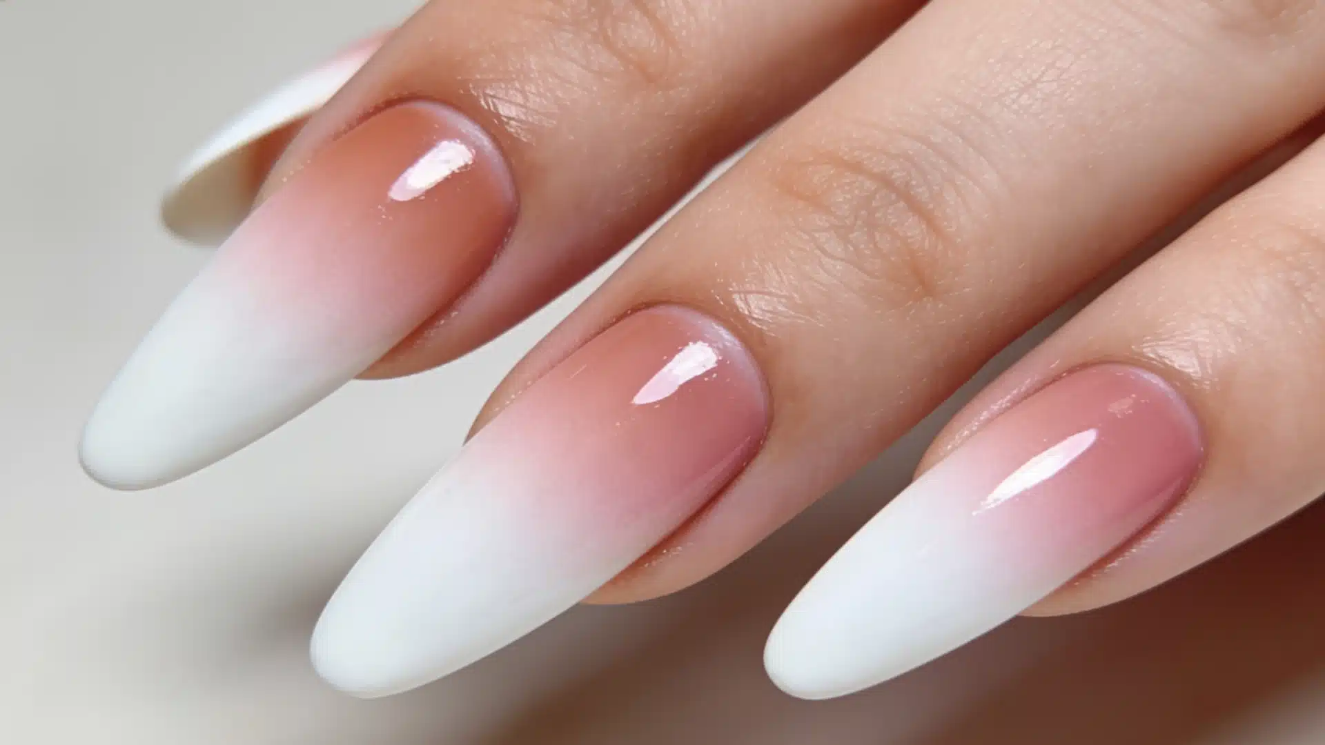 A woman's hand displaying elegant pink and white ombre nails with a smooth gradient and modern airbrushed finish