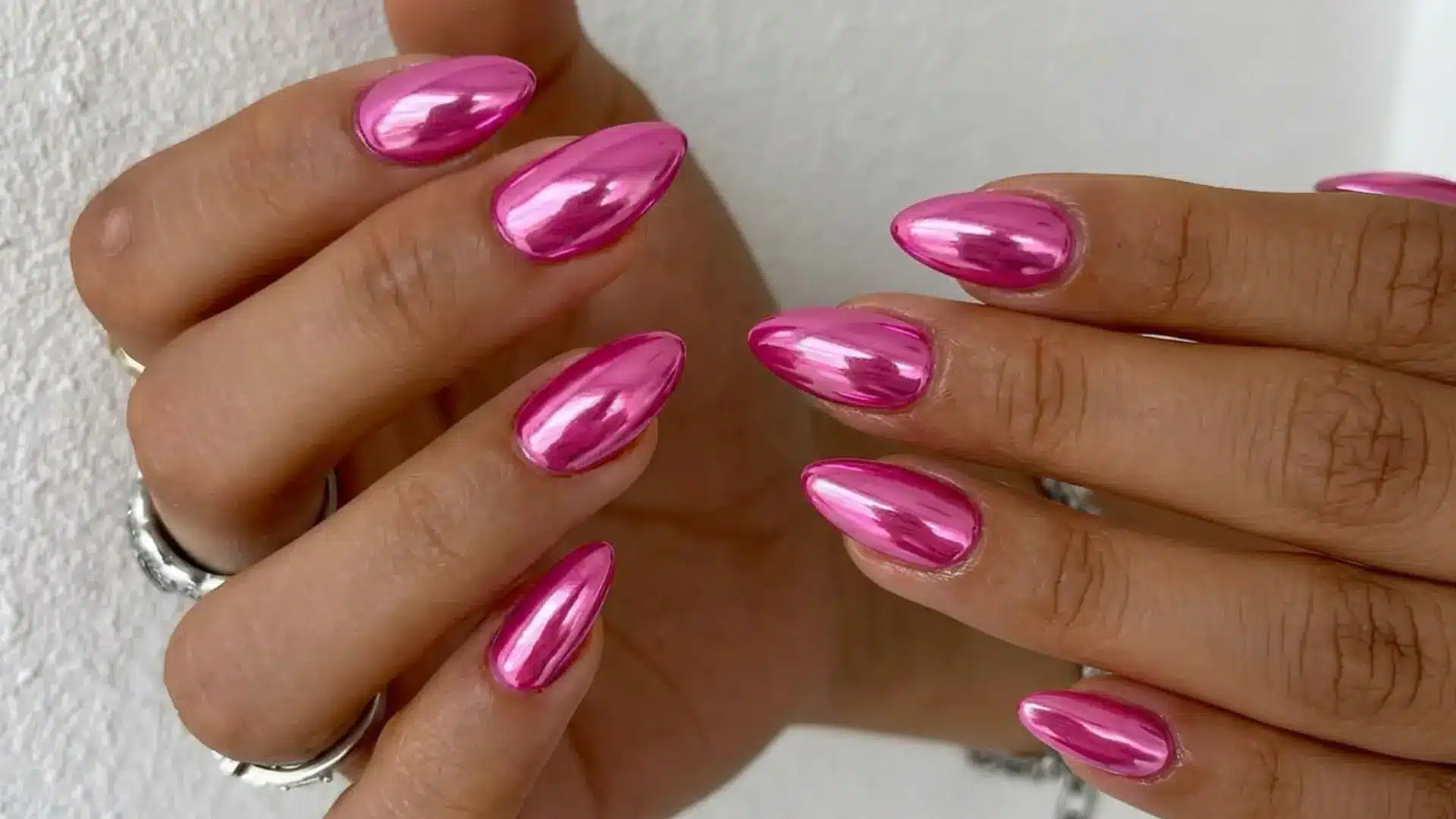 hot pink chrome almond nails with a full mirror metallic finish on both hands with silver rings