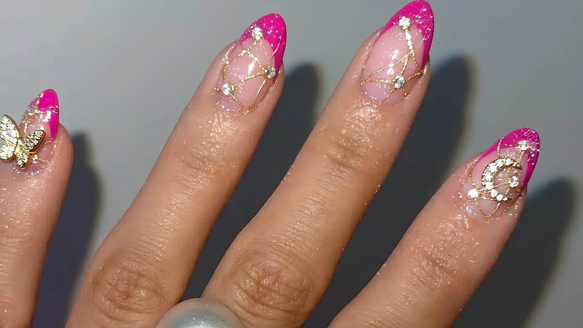 hot pink French tip almond nails with gold line art and crystal rhinestone accents on a nude base