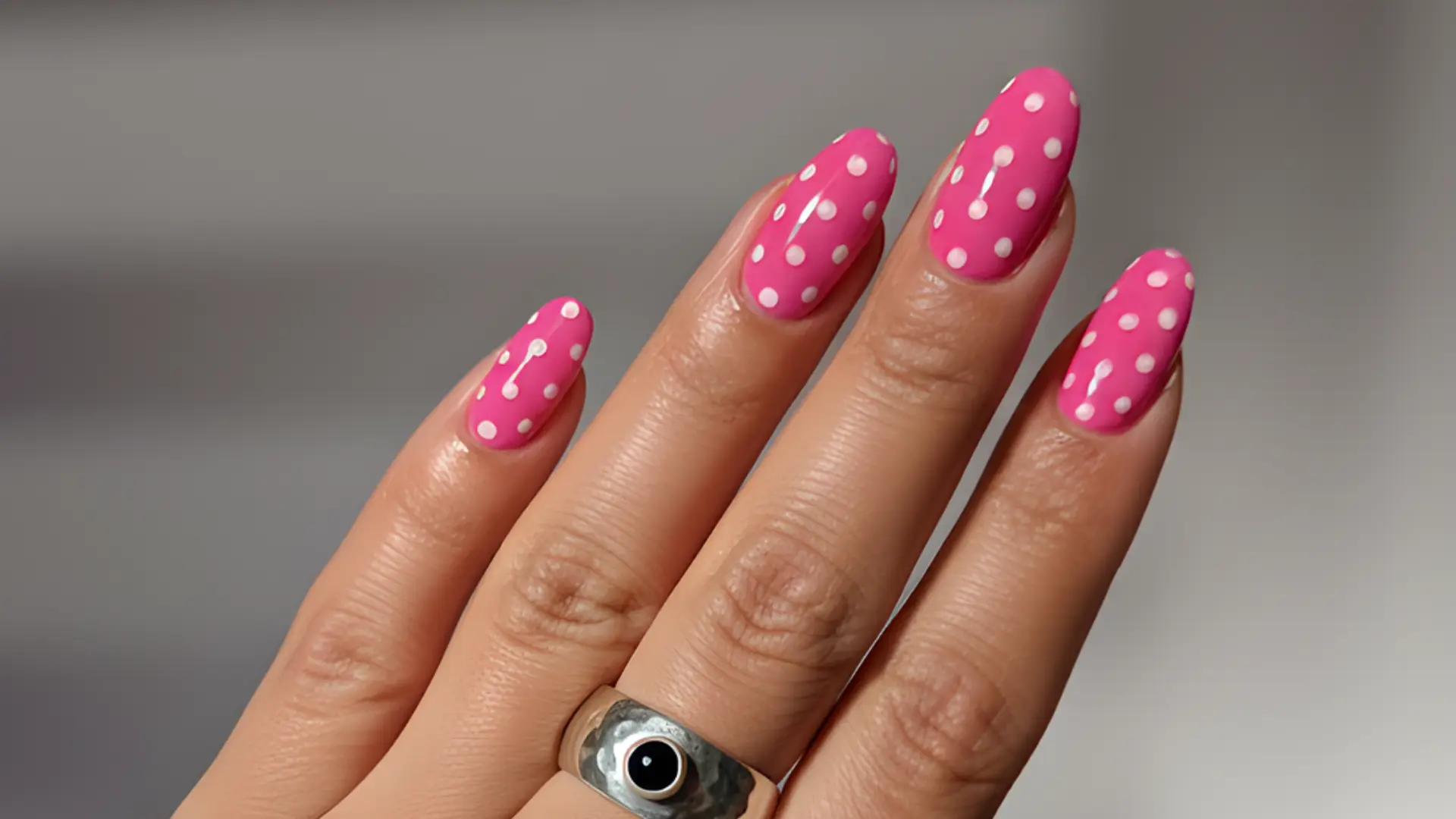 hot pink almond nails with white polka dots scattered across a glossy pink base with a silver ring