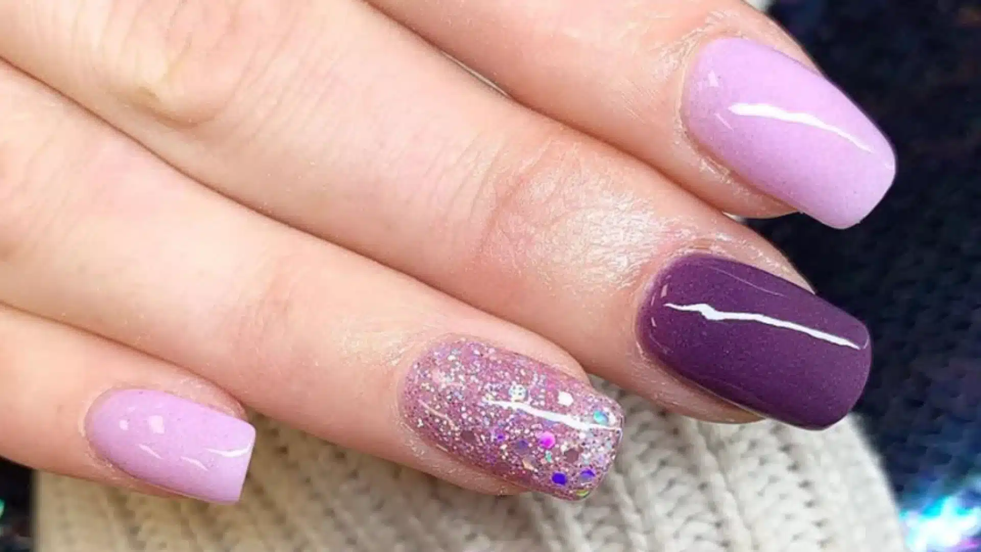 A woman's hand displaying purple and lavender SNS nails, showcasing a stylish manicure