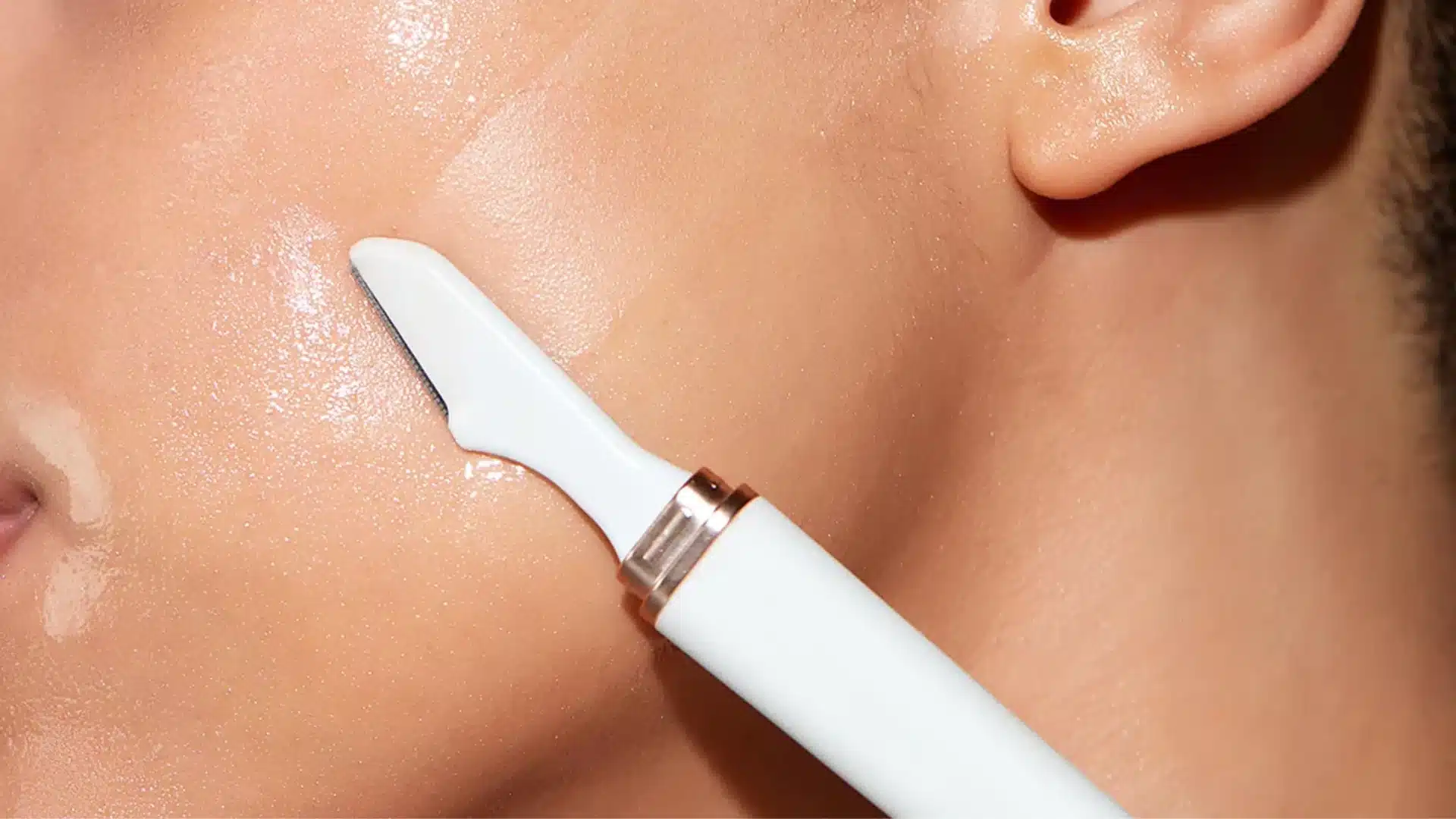 A close-up of a person's cheek with a white skincare tool touching their skin, highlighting a smooth, hydrated complexion.