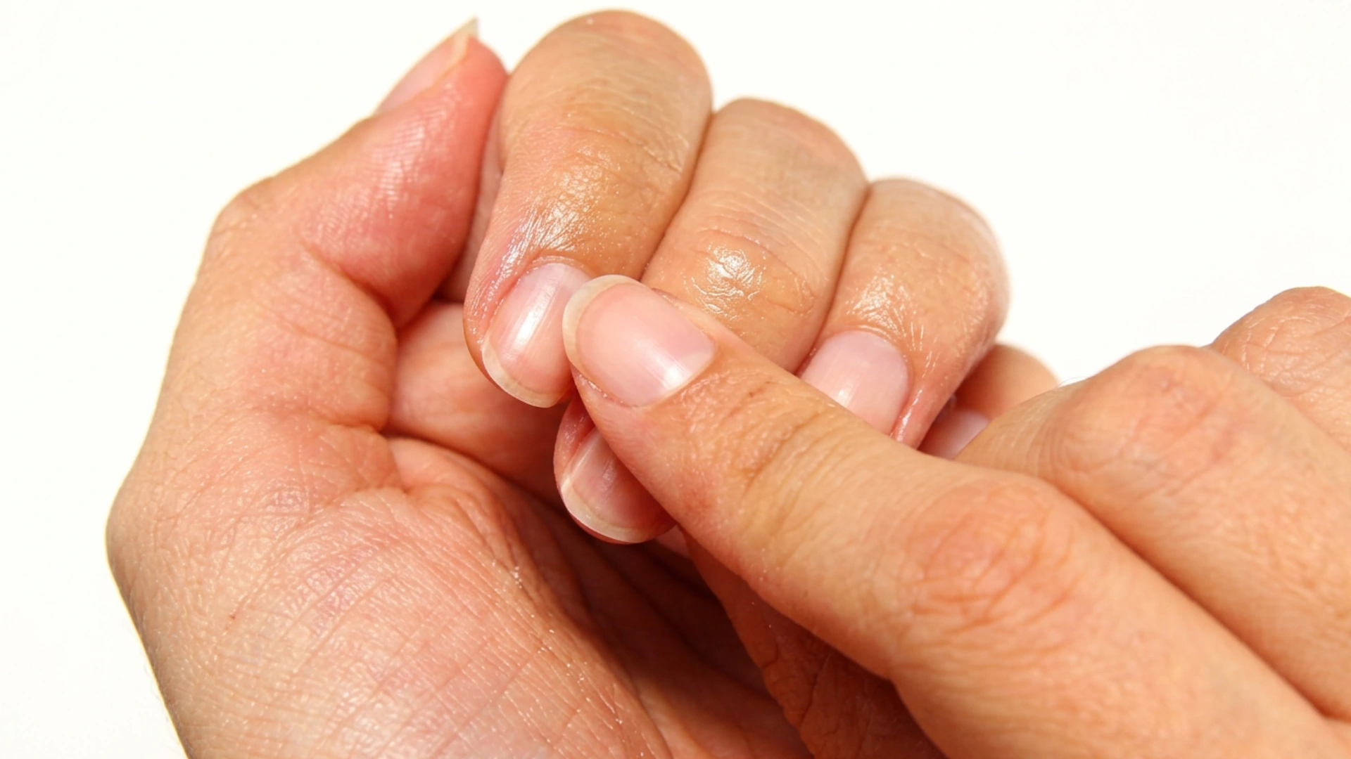 Close-up of natural fingernails and cuticles being gently massaged with fingertips after applying moisturizer, highlighting healthy, hydrated nails against a clean white background.