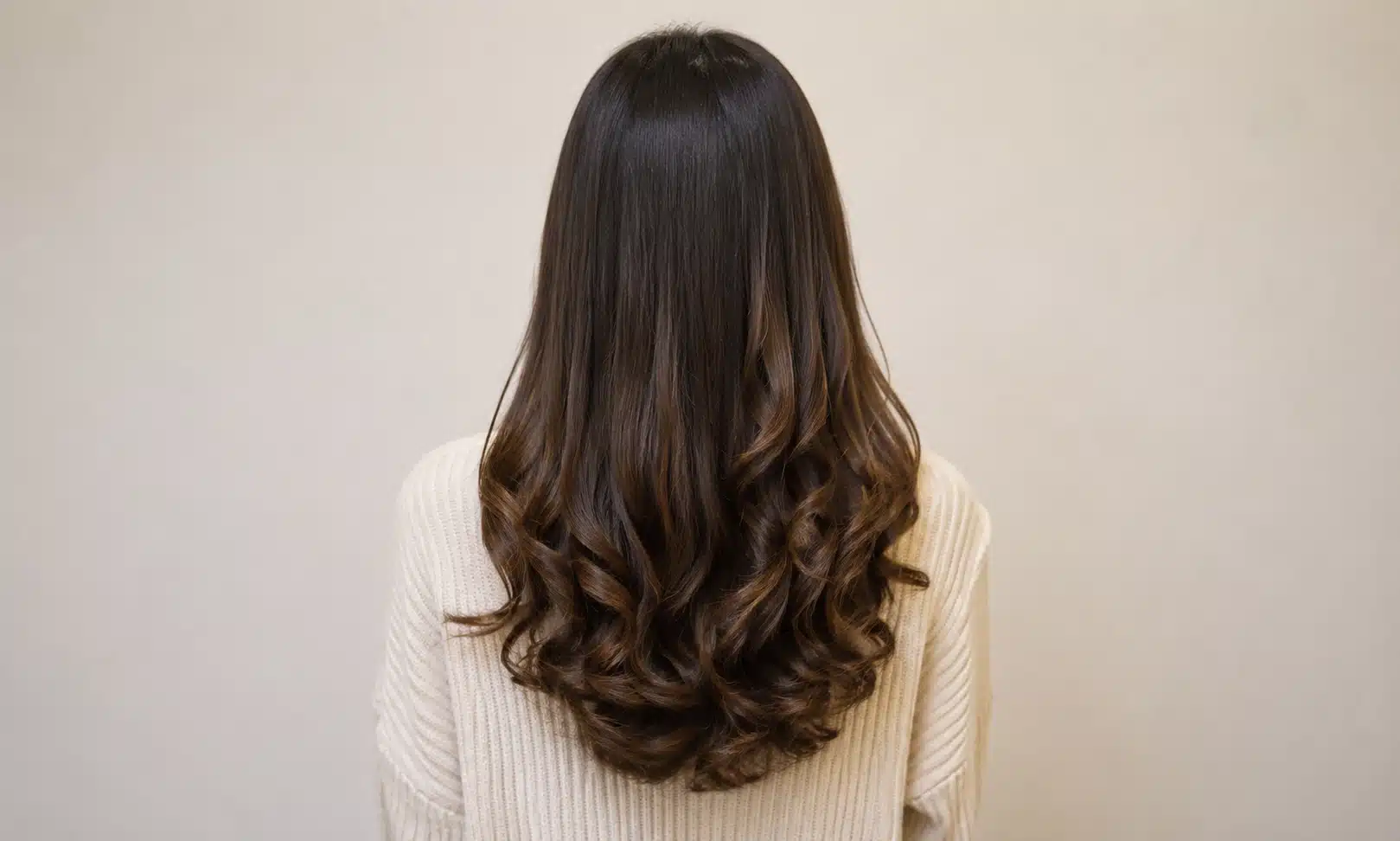 A woman with long, wavy hair is seen from the back, highlighting the flow and movement of her hair.
