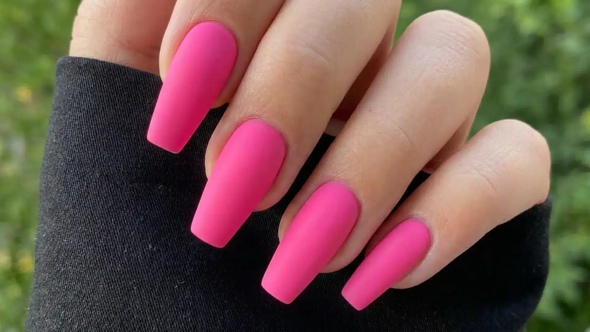 matte hot pink coffin nails with a smooth flat finish on long square shaped nails against a black sleeve
