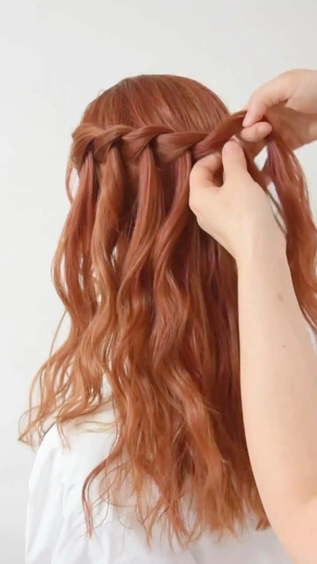 Waterfall braid being styled on wavy copper red hair