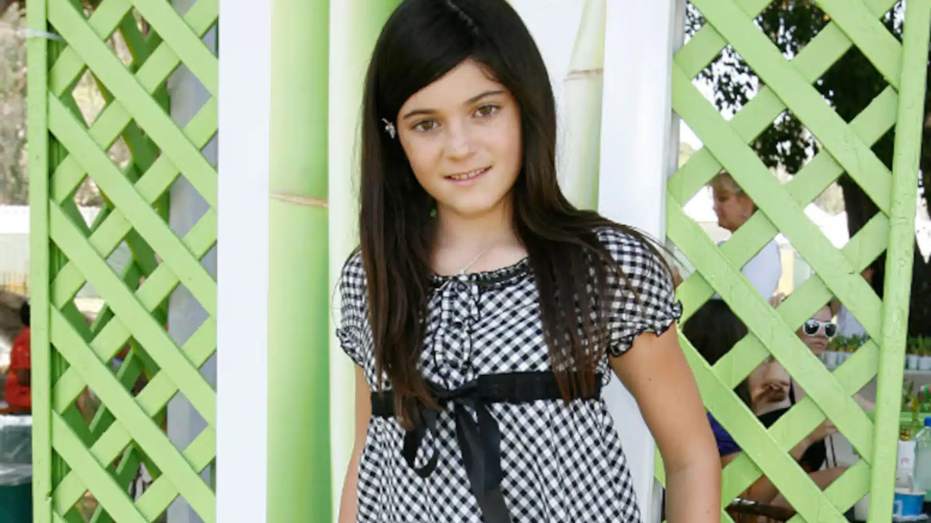 A young Kylie Jenner in a black and white dress poses happily, highlighting her joyful expression and stylish outfit.