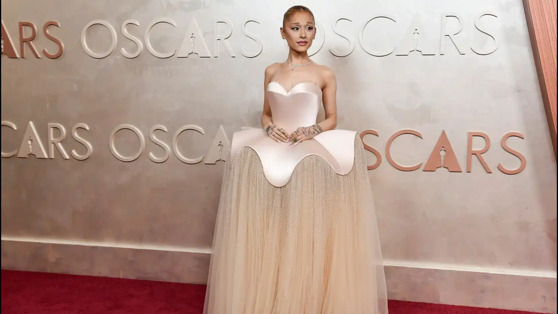 Ariana Grande poses in a strapless white gown on the Oscars red carpet in front of an Oscars-branded backdrop