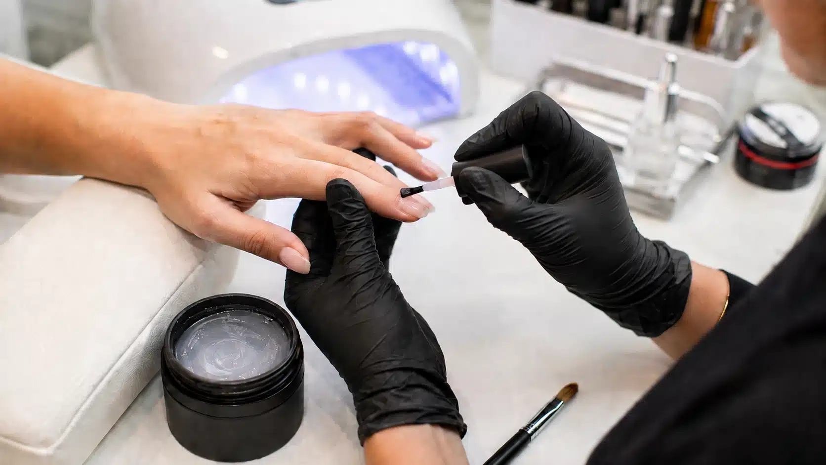 Nail technician applies pale builder gel directly to a client’s fingernail at a clean salon manicure station
