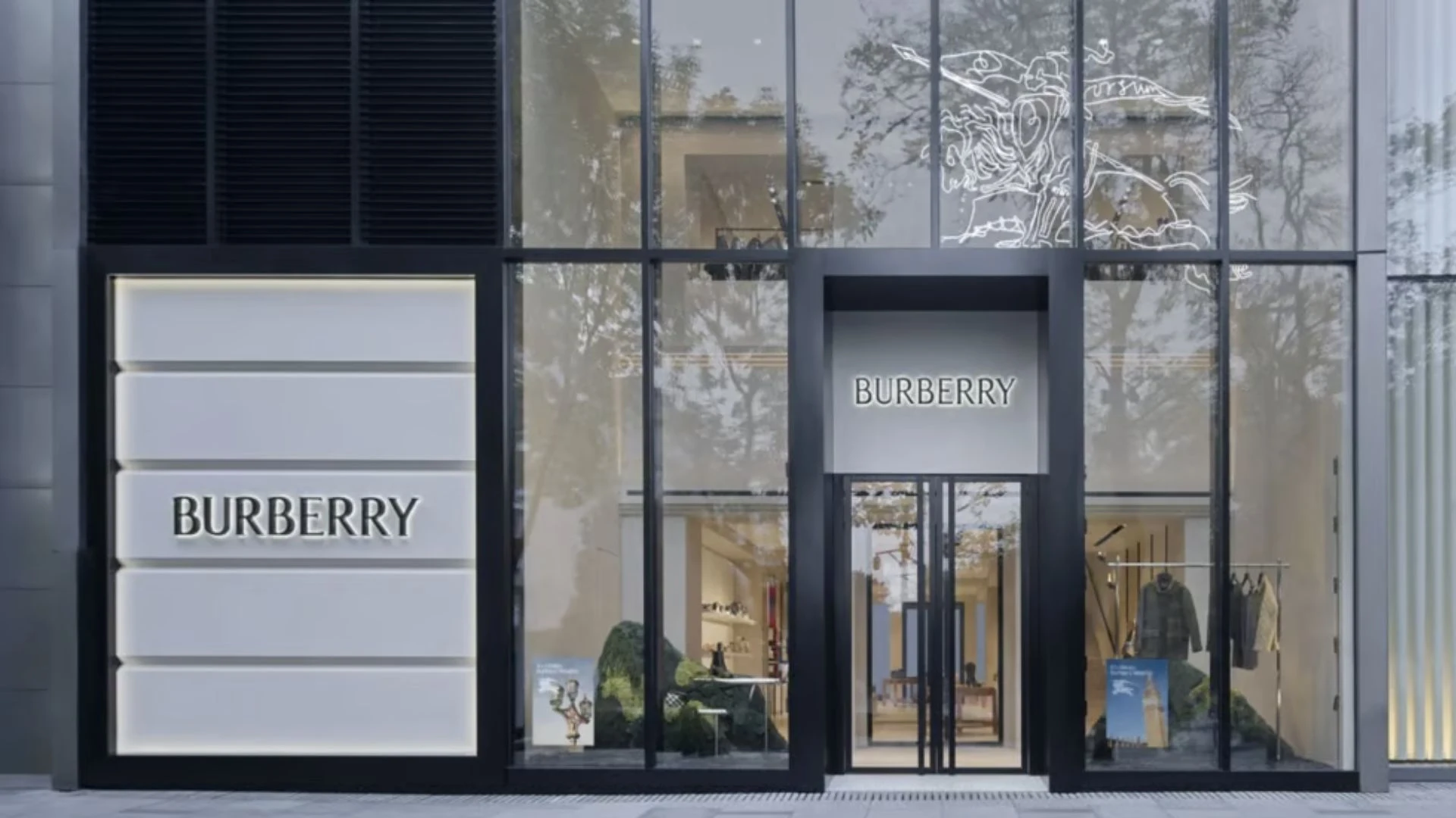 Burberry store entrance with illuminated brand signage, glass windows, and clothing displays visible inside.