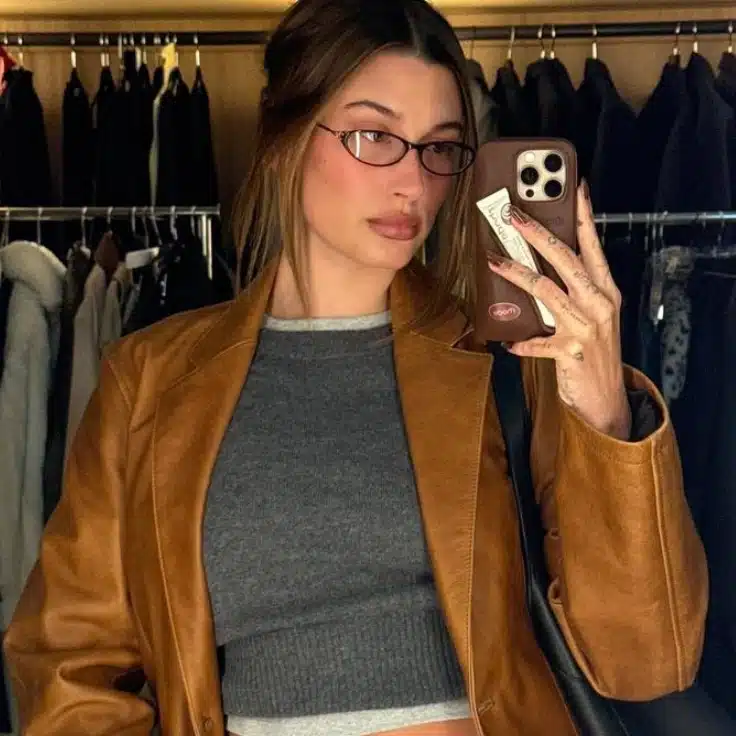 Hailey Bieber wearing cat eye glasses, taking a selfie in front of a mirror.