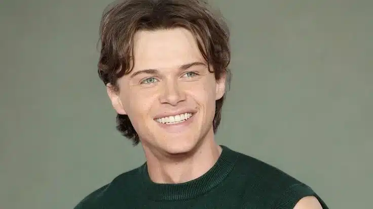 Christopher Briney with brown hair, wearing a green shirt, smiles warmly at the camera.