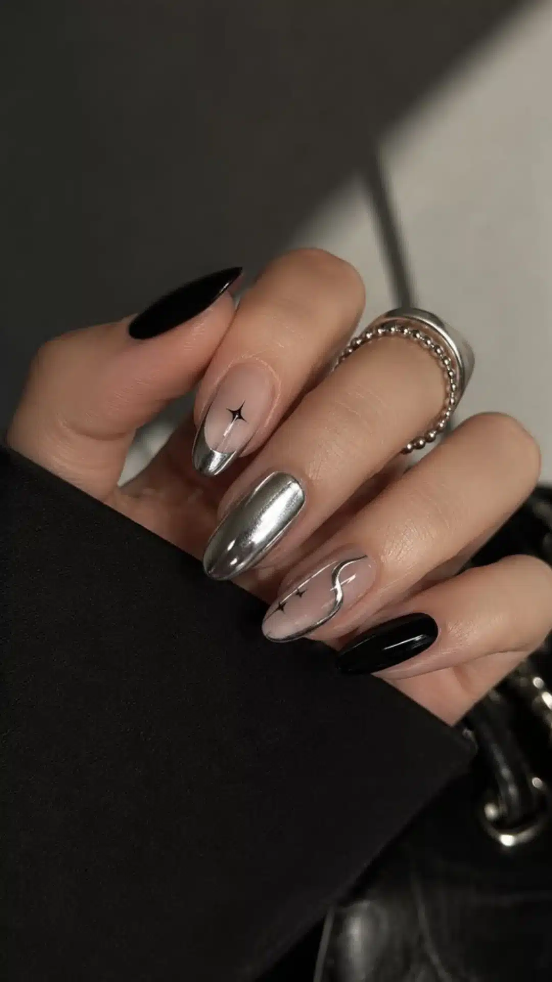 A woman with black and silver nails holds a stylish black purse, showcasing her fashionable accessories