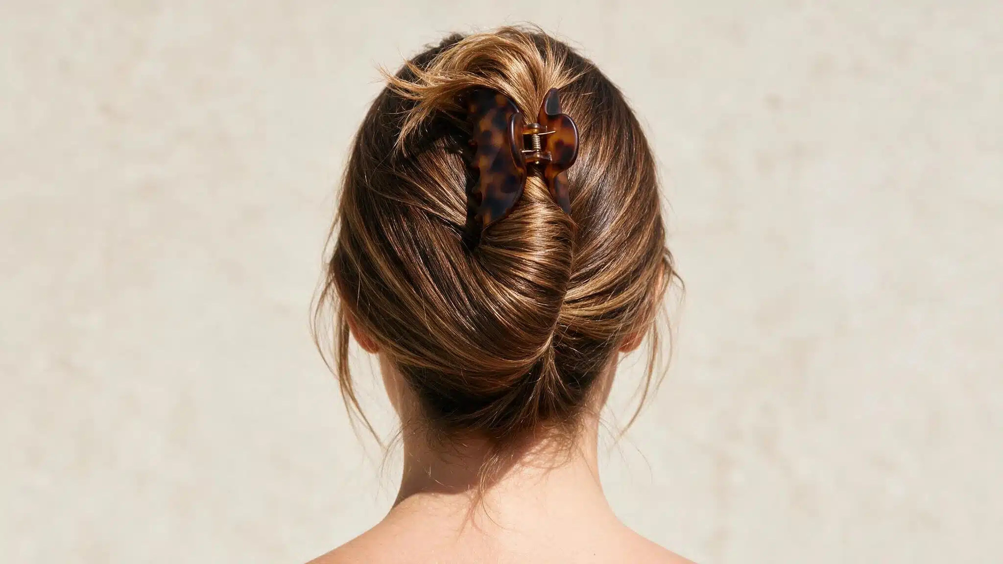 woman with medium-to-long hair wearing a claw-clip French twist secured vertically at the back with a large clip