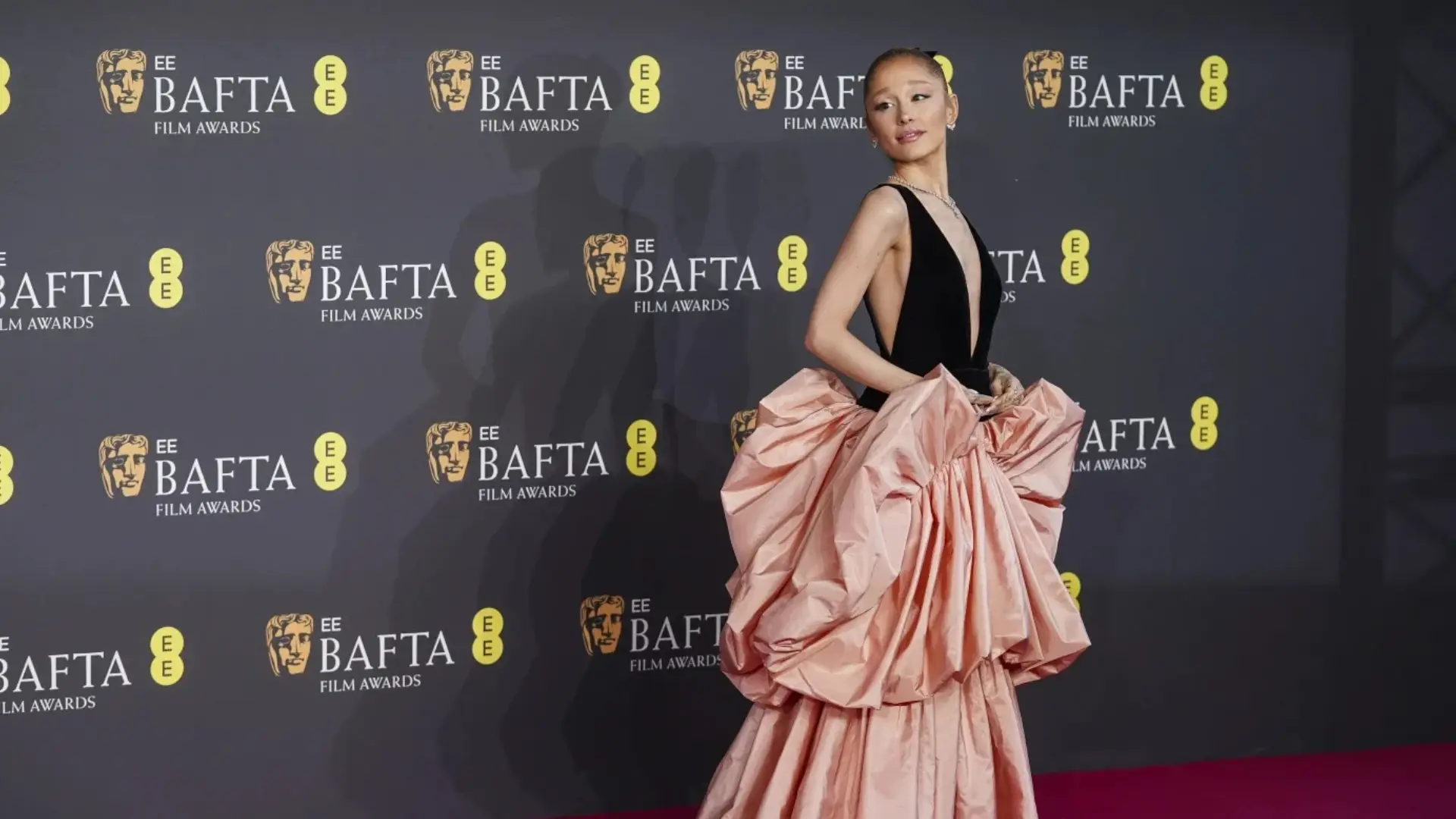 A woman poses in a black sleeveless top and voluminous blush-pink gown on the BAFTA Film Awards red carpet.