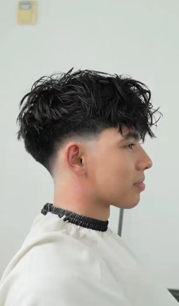 Drop fade haircut with a textured curly top and a fade that curves behind the ears