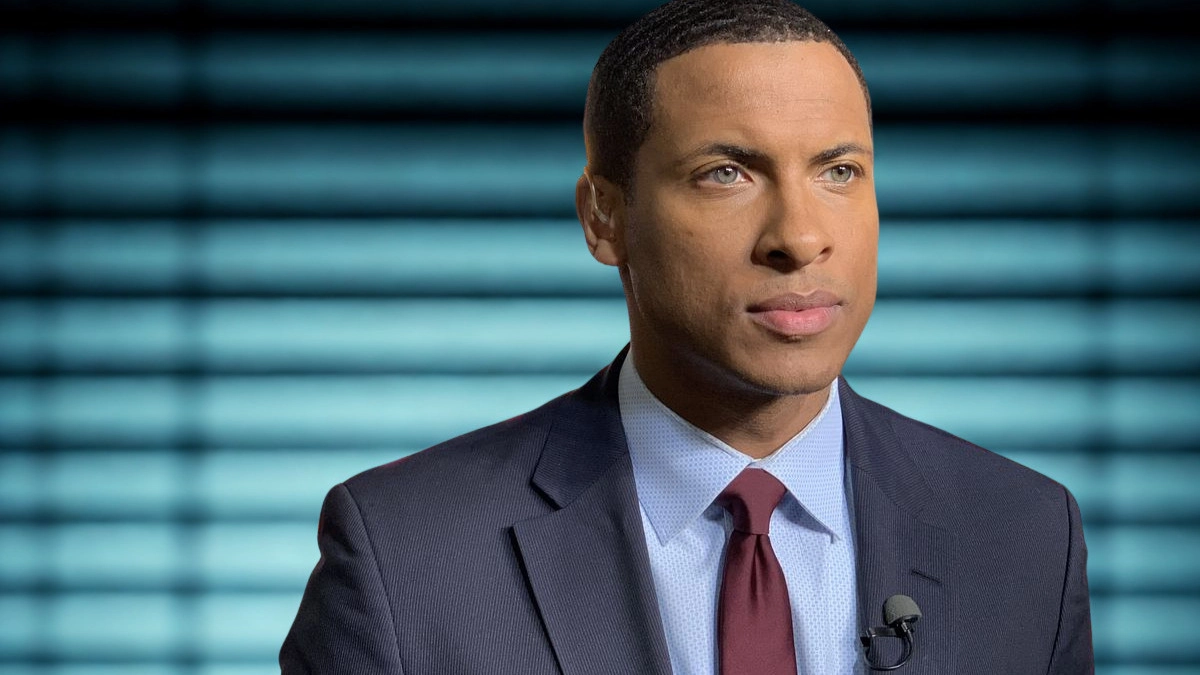 Errol Barnett in a suit and tie gazes thoughtfully to the side, exuding professionalism and poise.