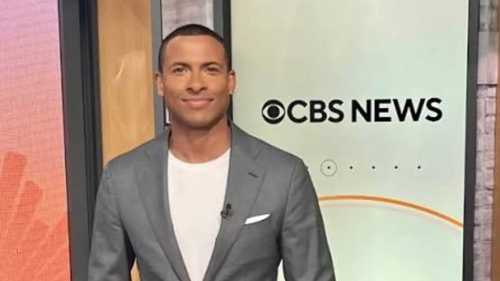 Errol Barnett wearing a gray suit during a CBS News studio appearance while smiling at the camera in front of the CBS News logo