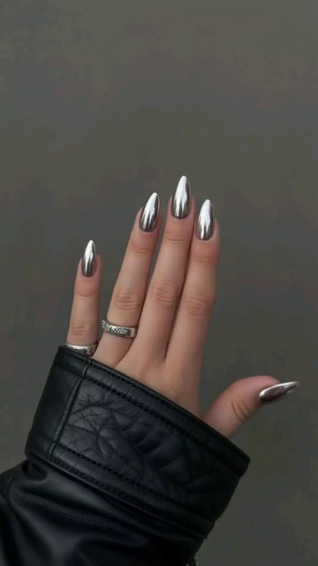 A close-up of a woman's hand with full mirror chrome nails, resting on a black leather jacket
