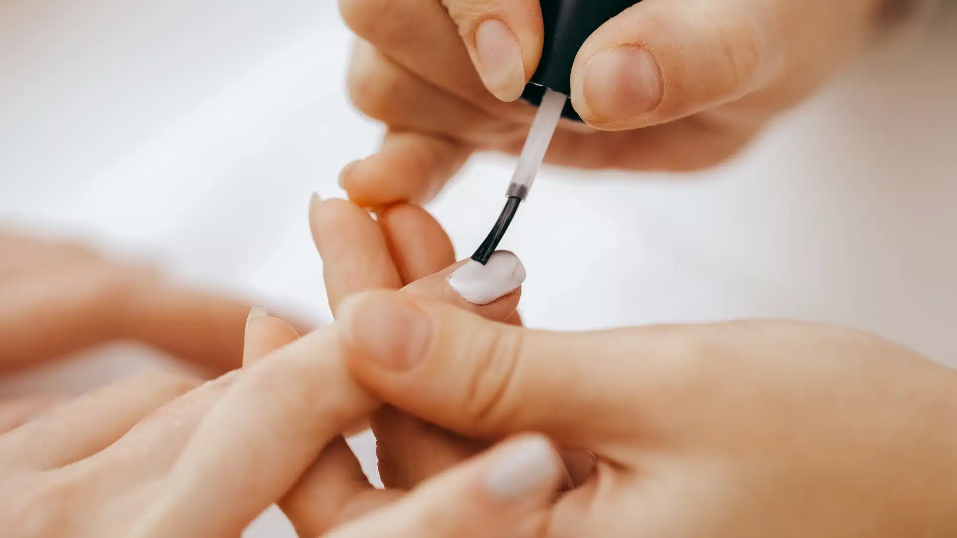 Applying a white base color coat to the nail with a polish brush before starting the ombre fade