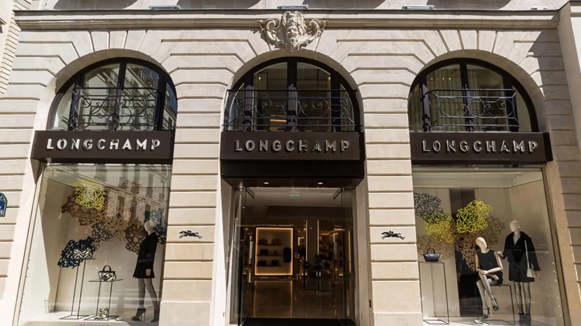 Longchamp luxury boutique with three arched storefront windows, handbags displayed in the showcases, and mannequins outside the entrance.