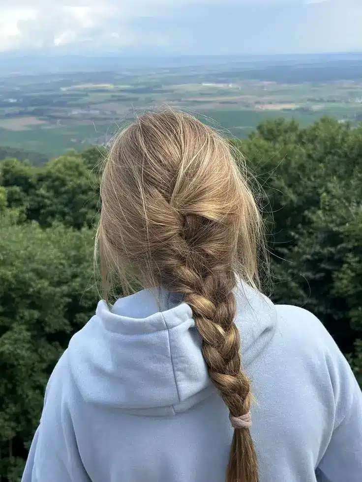 Back view of blonde hair styled in a loose side braid with soft face framing strands creating an effortless hairstyle that helps disguise greasy hair