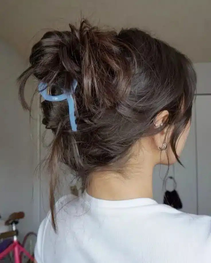 Dark brunette hair gathered into a messy claw clip bun with loose face framing pieces creating a casual hairstyle that disguises greasy hair naturally