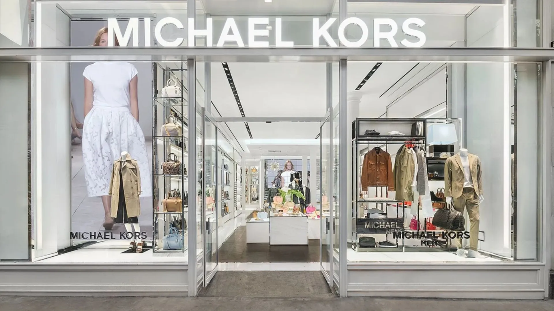 Michael Kors store entrance displaying mannequins in clothing, handbags, and accessories behind glass storefront windows.