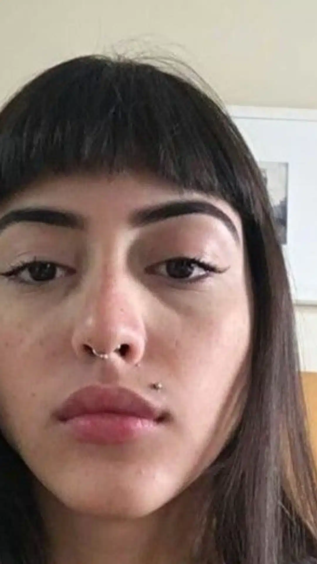 Close-up portrait of a person with a septum ring and a Monroe piercing above the upper lip on the right side.