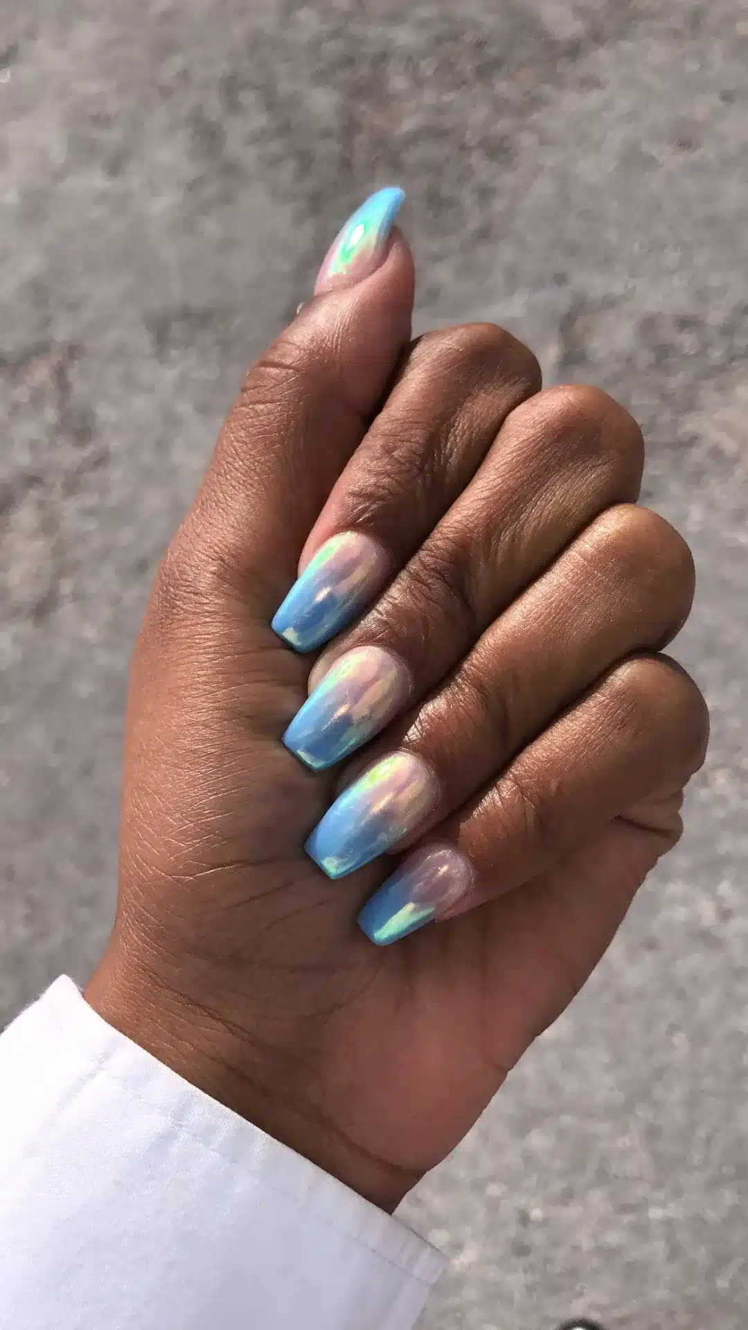 A hand with blue and white painted nails is raised, emphasizing the vibrant colors and nail style