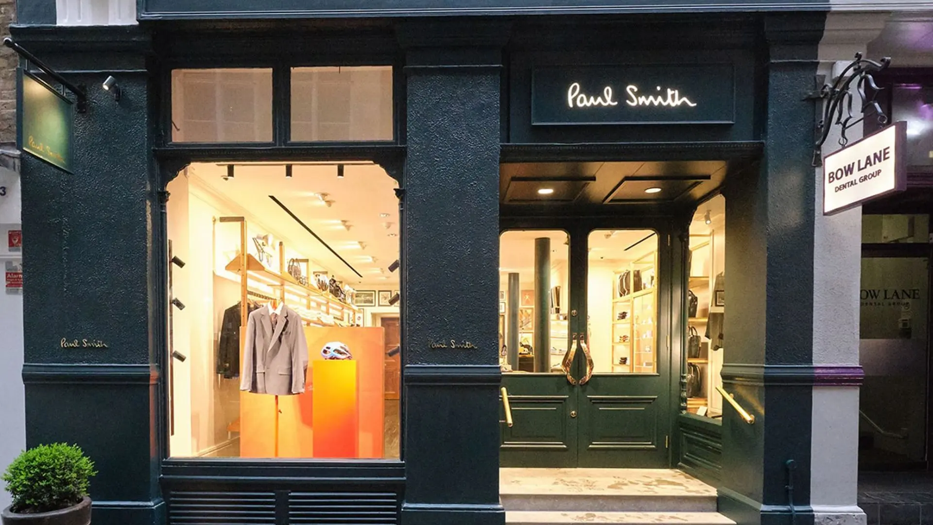 Paul Smith clothing boutique with dark green storefront, illuminated display windows, and open entrance beside Bow Lane Dental Group.