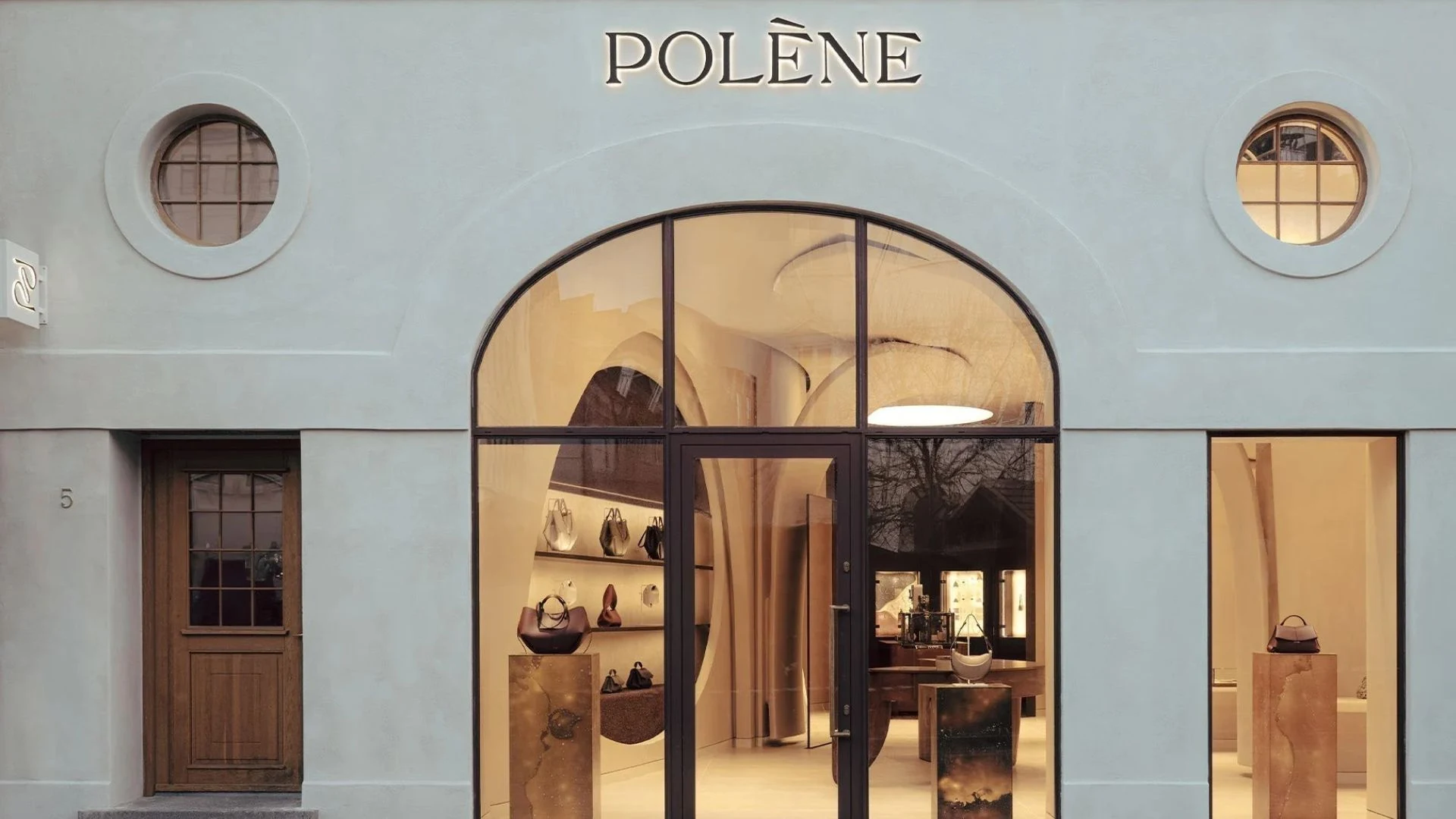 Polène handbag boutique storefront with pale blue walls, arched glass entrance, circular windows, and handbags displayed inside.
